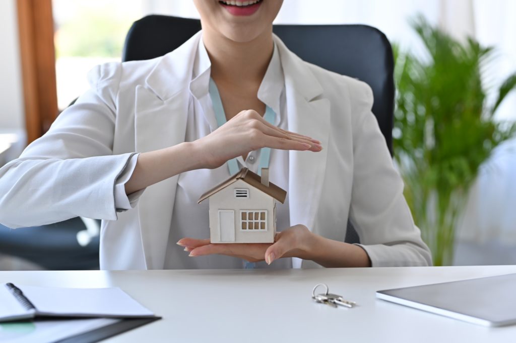 Cropped shot young woman hand protecting house model. Insurance or loan real estate concept.